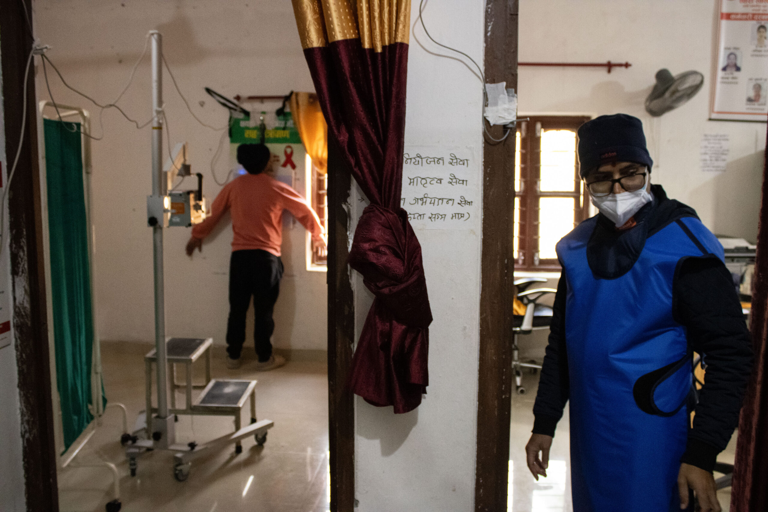 A radiographer in protective gear standing by as a patient is positioned for a chest X-ray with the Delft Light system at a health facility in Nepal.